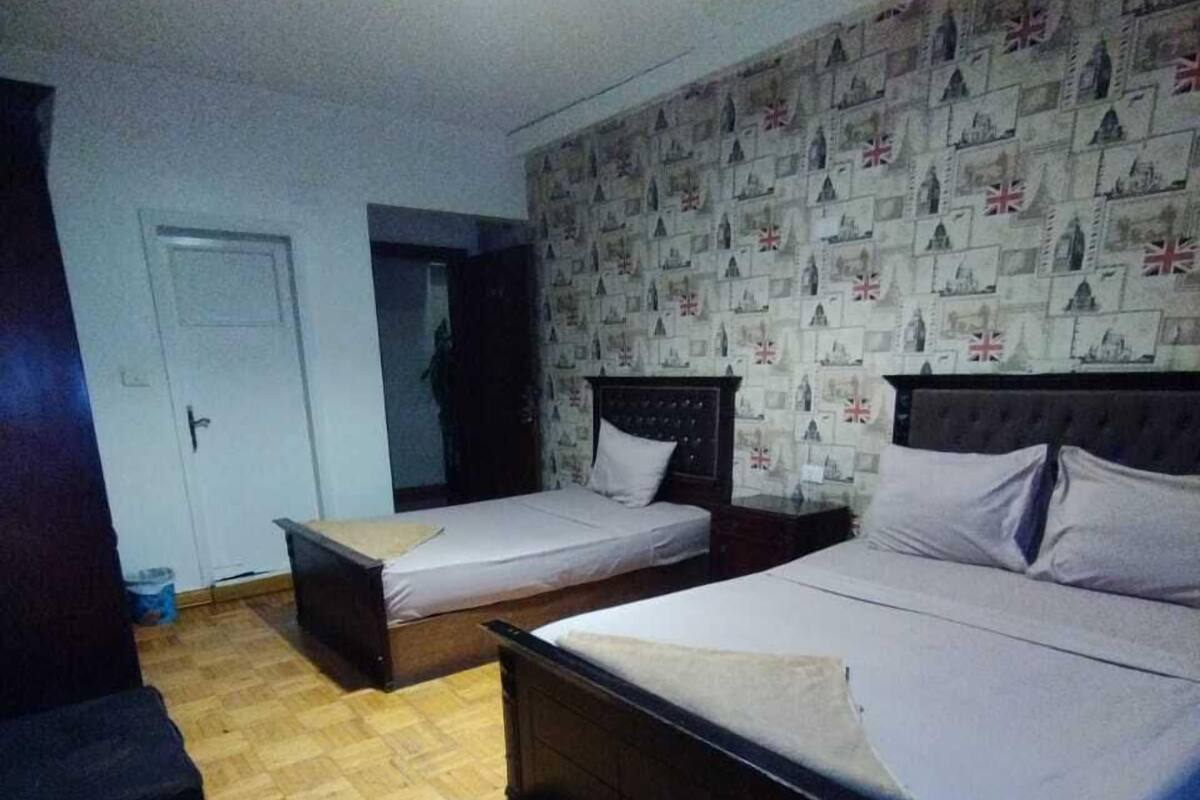 A room with two single beds, a wooden floor, and a wall with a pattern of buildings and flags.