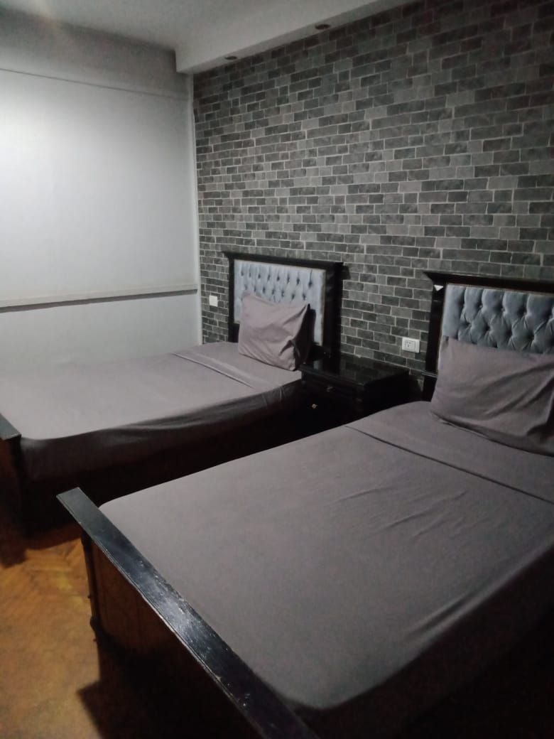 Deux lits simples avec des têtes de lit, un mur en briques et un plafond blanc.