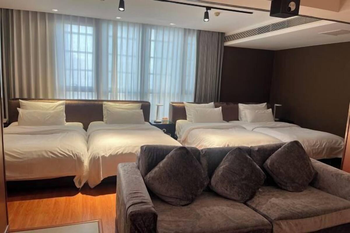 A hotel room with two beds, a sofa, and a large window with curtains.