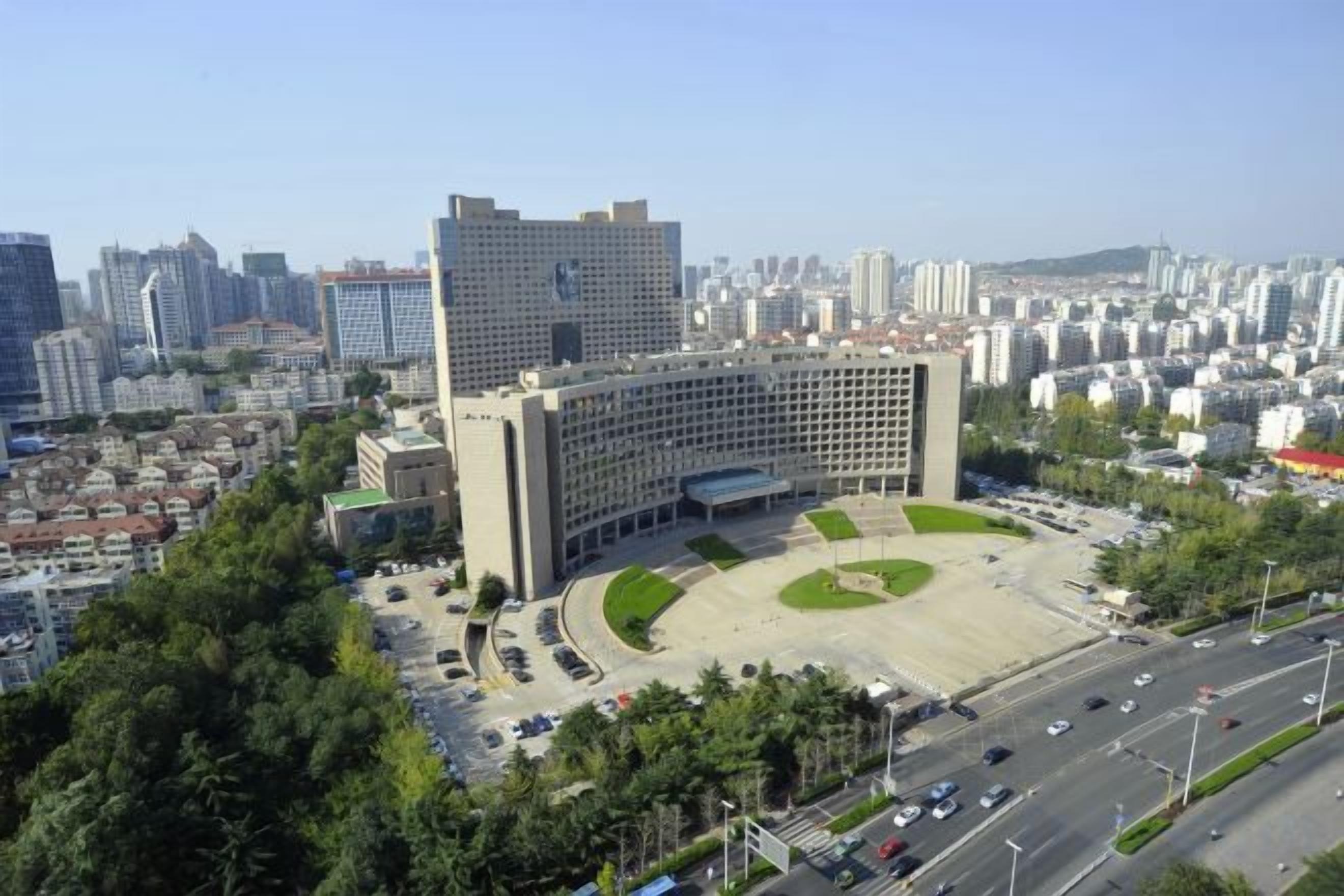 A large building with a central courtyard surrounded by trees, set in a densely populated urban area with high-rise buildings in the background.