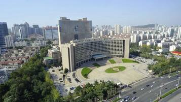 A large building with a central courtyard surrounded by trees, set in a densely populated urban area with high-rise buildings in the background.