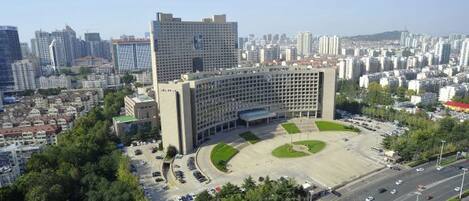 A large building with a central courtyard surrounded by trees, set in a densely populated urban area with high-rise buildings in the background.