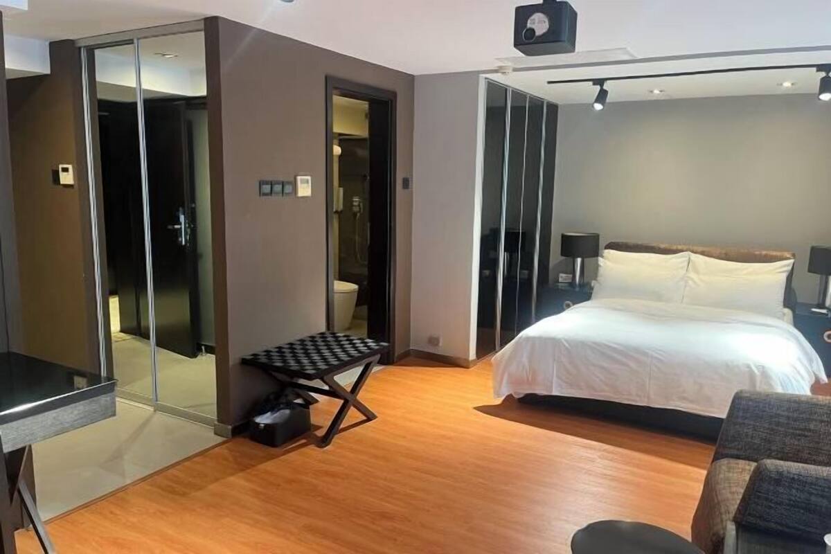 A hotel room with a bed, a desk, a chair, a small table, and a sliding door leading to a bathroom.