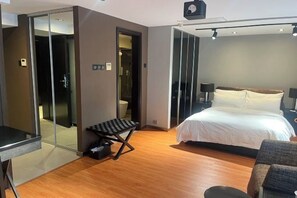 A hotel room with a bed, a desk, a chair, a small table, and a sliding door leading to a bathroom. - Housing International Hotel (Qingdao)