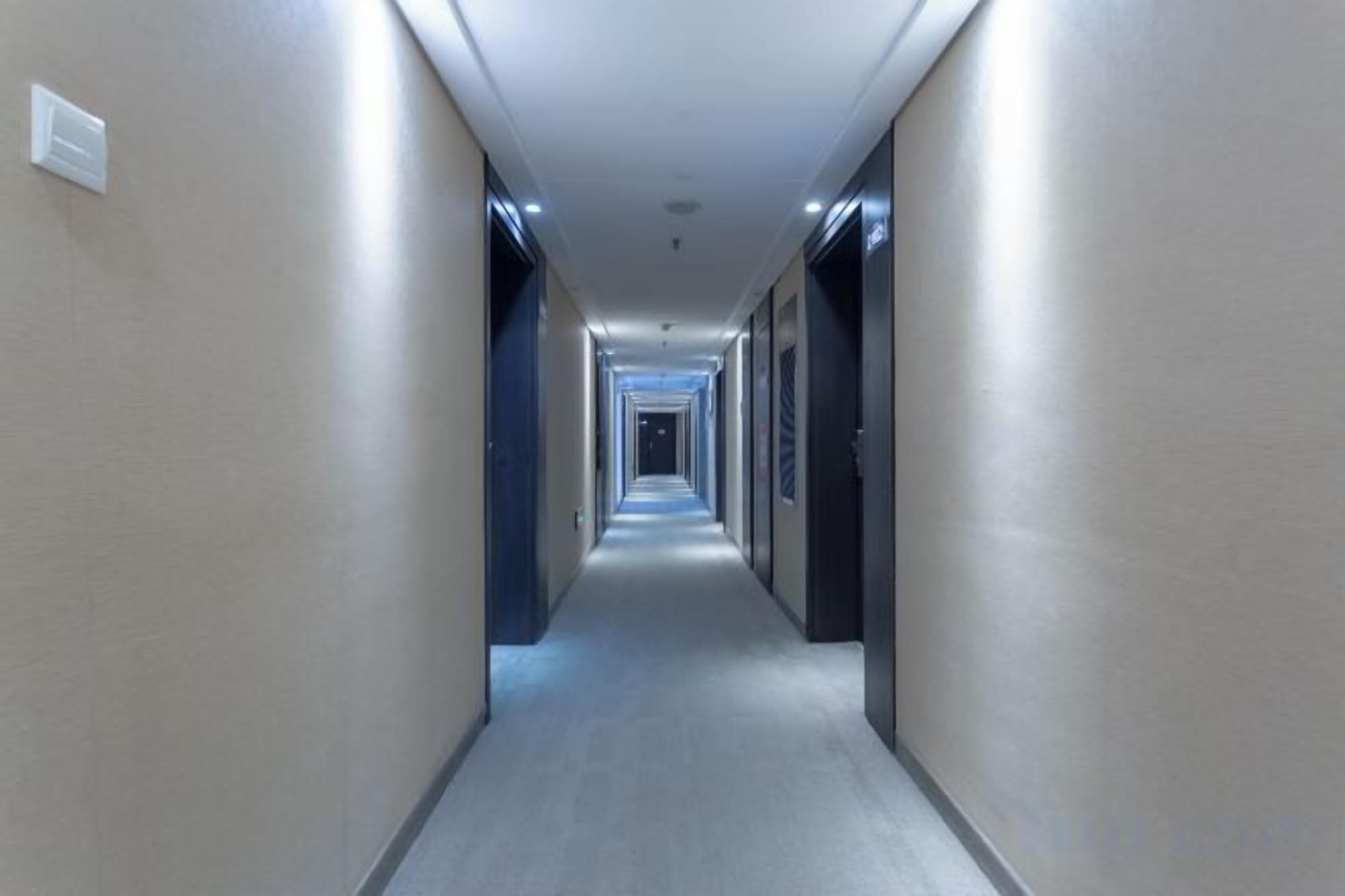 A long, narrow hotel corridor with doors on both sides and a carpeted floor.