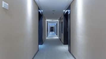 A long, narrow hotel corridor with doors on both sides and a carpeted floor.