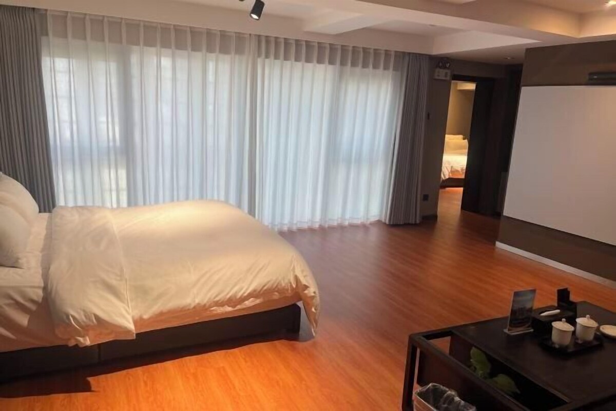A modern hotel room with a large bed, wooden flooring, and a small table with decorative items.