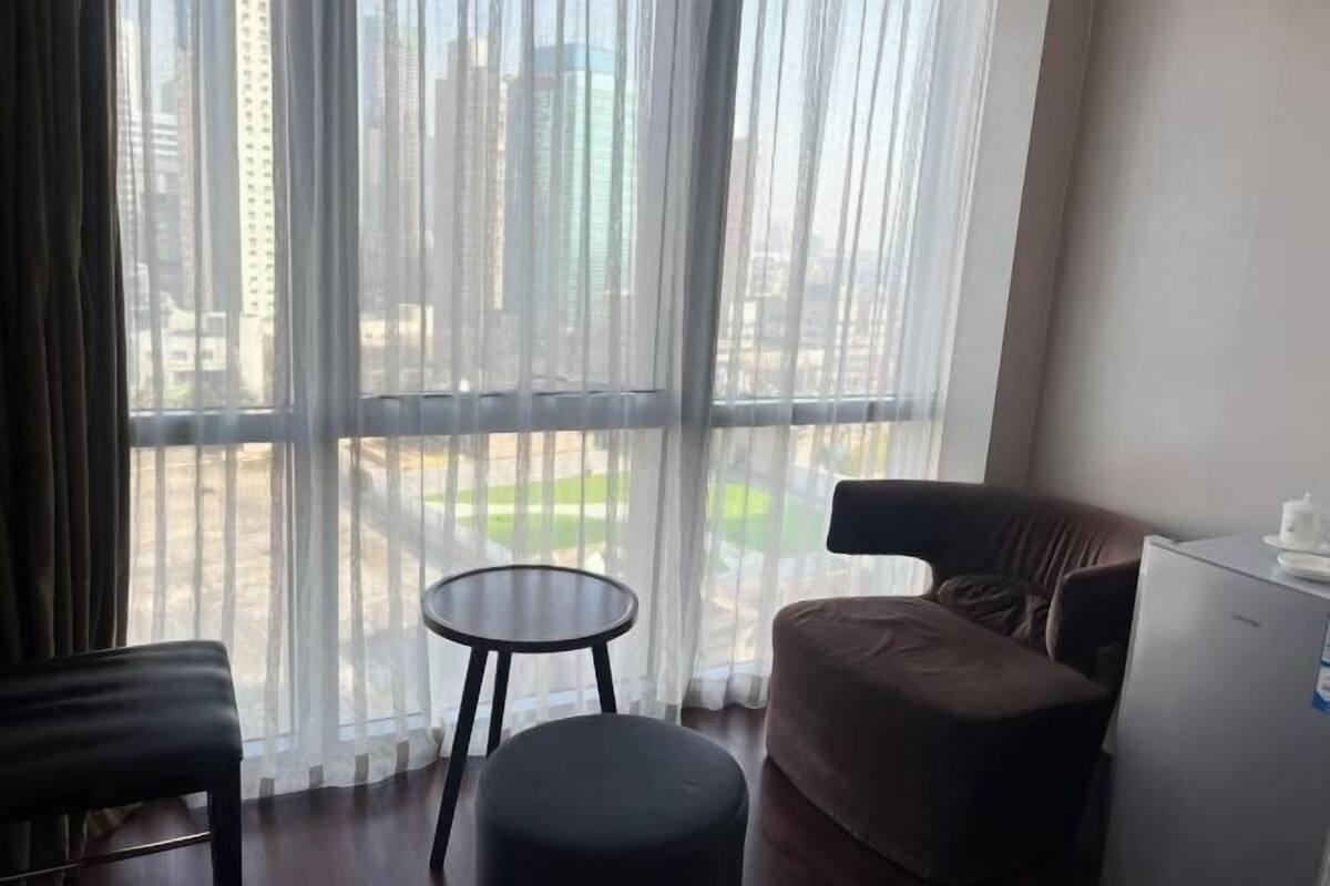 A room with a large window, a small round table, a sofa, and a refrigerator.