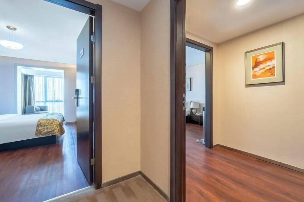 A hotel room with a bed, a window with curtains, a door leading to another room, and a framed picture on the wall.