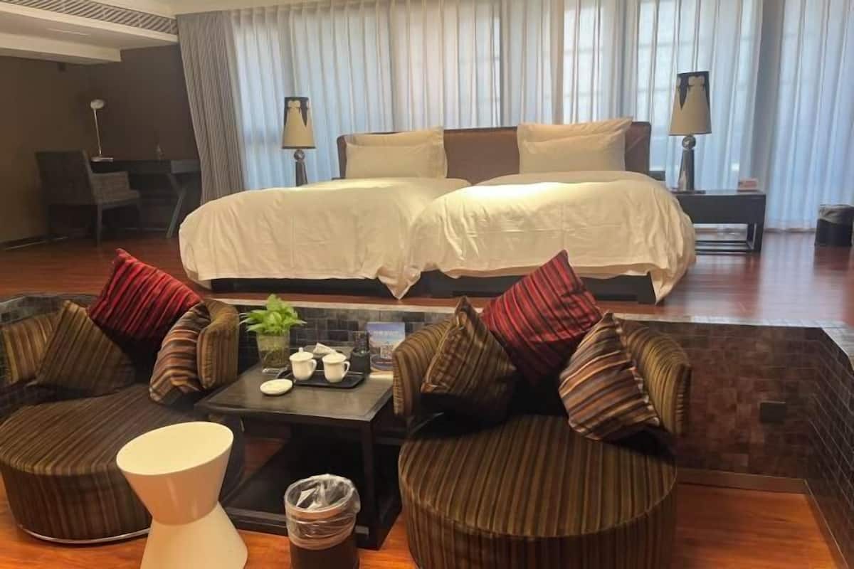 A hotel room with a double bed, two bedside tables with lamps, a sofa, a coffee table with a tray of items, and a trash bin.