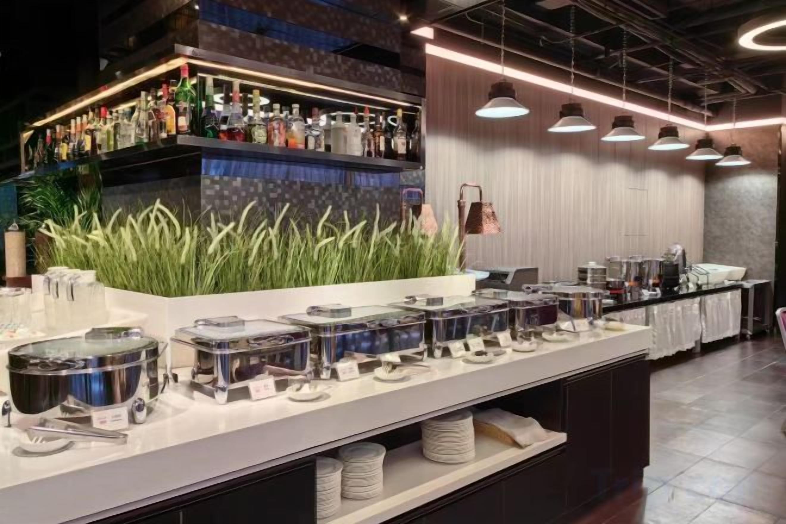 A buffet setup with various food containers, a bar area with bottles, and a seating area with tables and chairs.