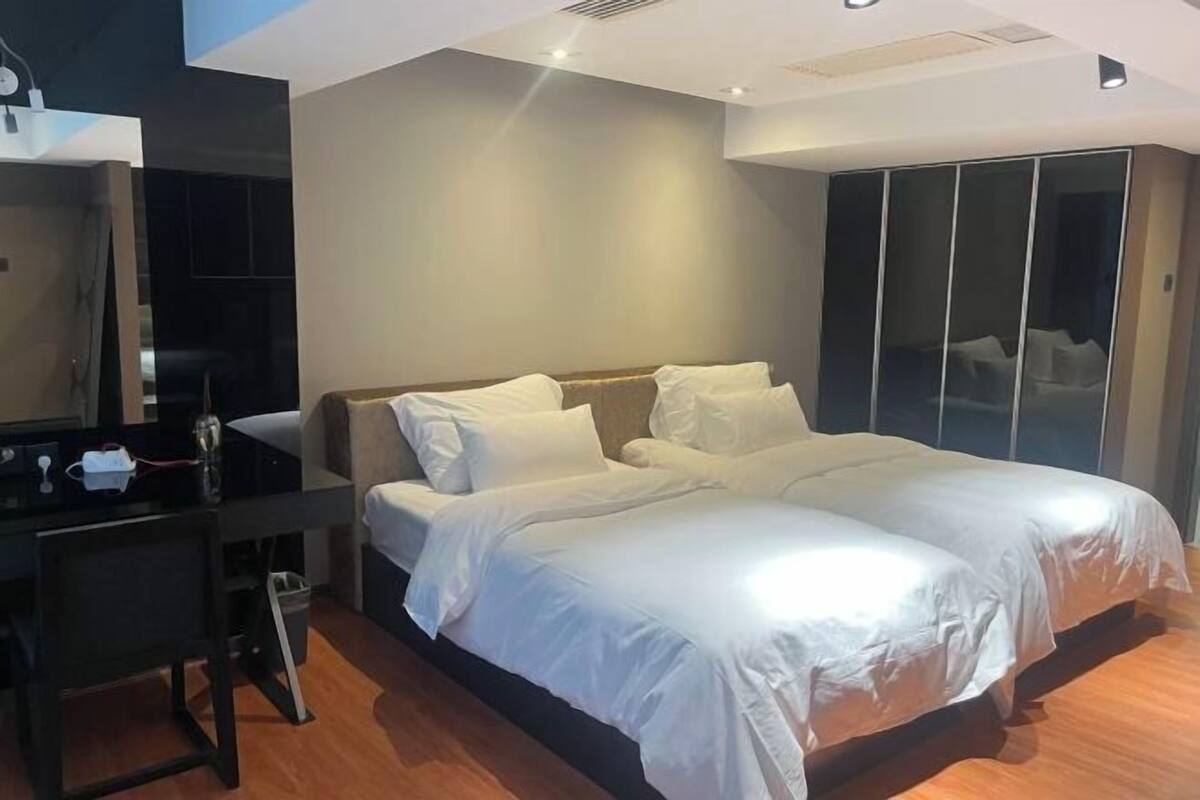 A modern hotel room with a large bed, a desk with a chair, and a wardrobe.