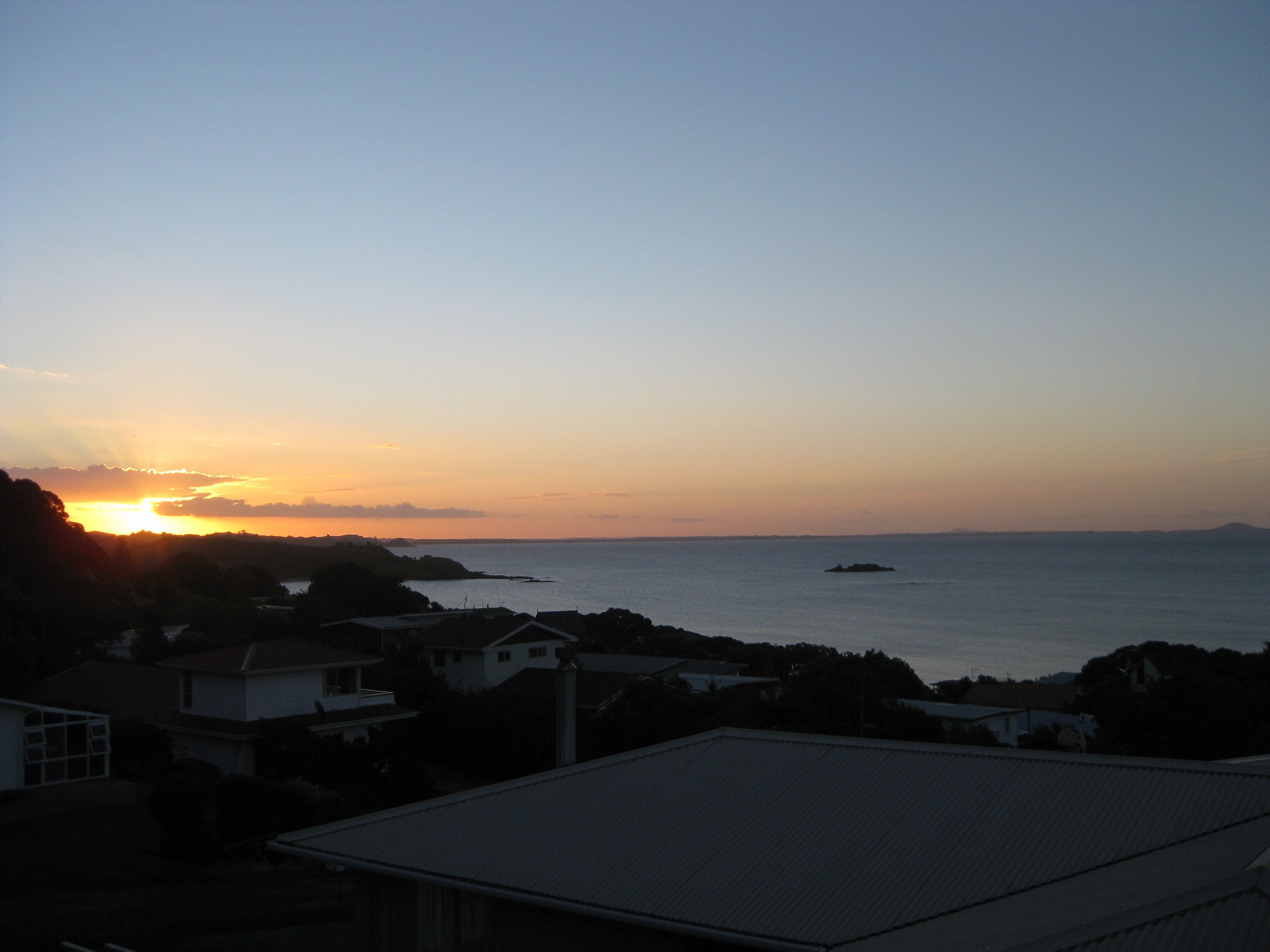 A coastal sunset view with houses in the foreground and a small island in the distance.