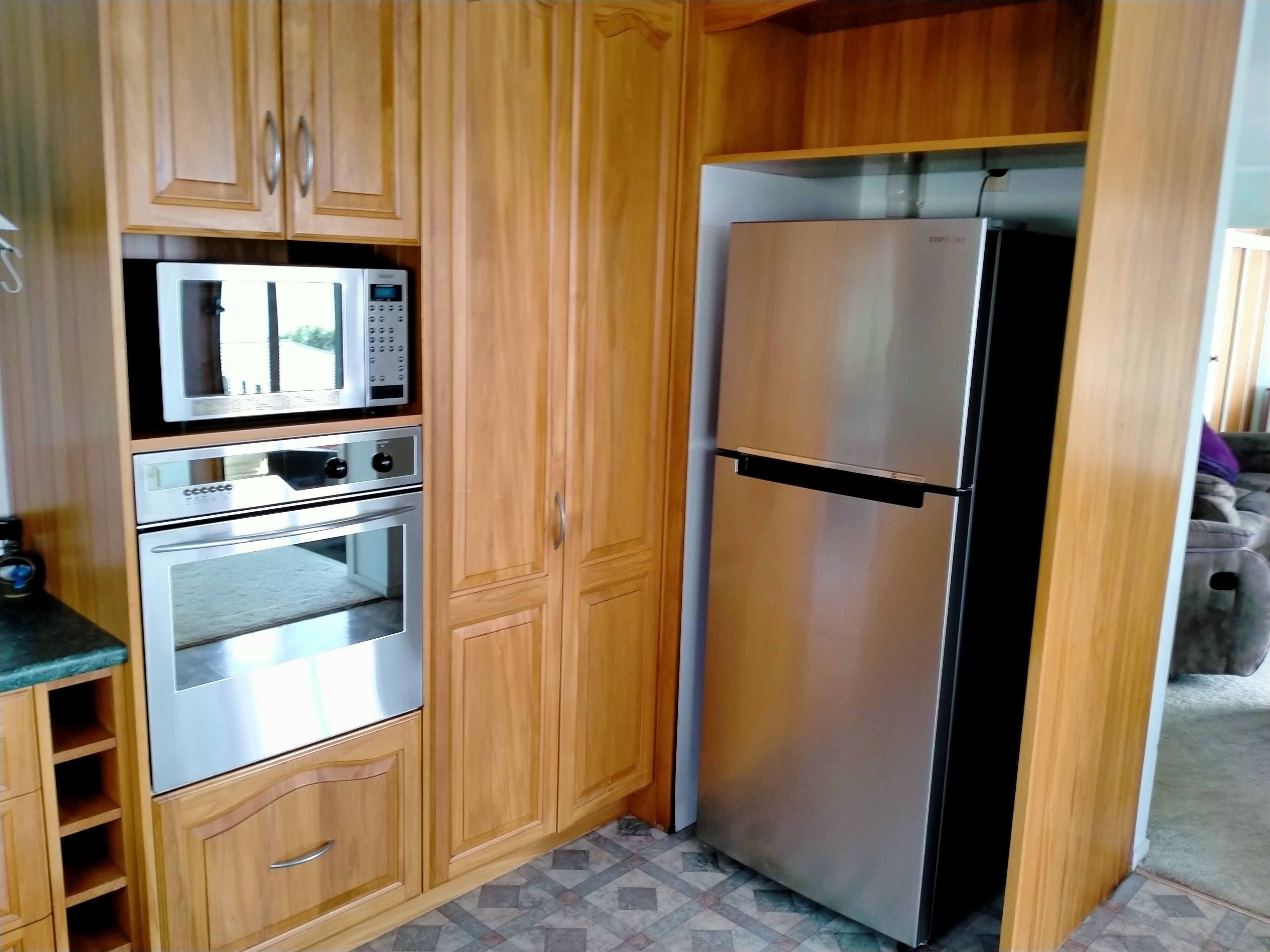 Een kleine keuken met houten kastjes, een magnetron, een oven en een koelkast van roestvrij staal.