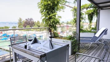 A balcony with a table set for dining, a lounge chair, and a view of a body of water with boats.