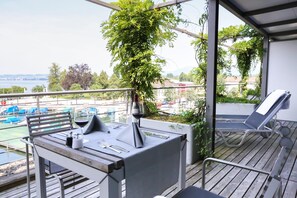 A balcony with a table set for dining, a lounge chair, and a view of a body of water with boats.