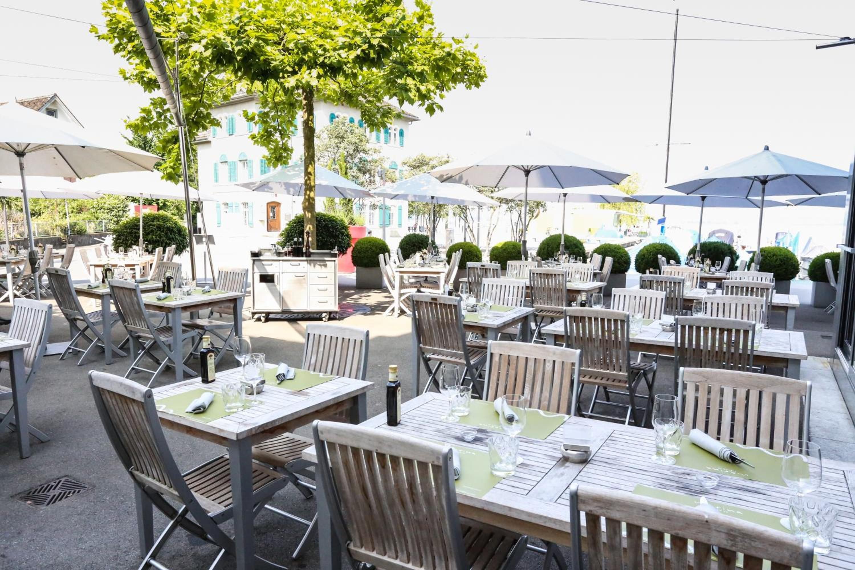Un espace extérieur aménagé pour les repas, avec des tables, des chaises, des parasols et un bâtiment en arrière-plan.