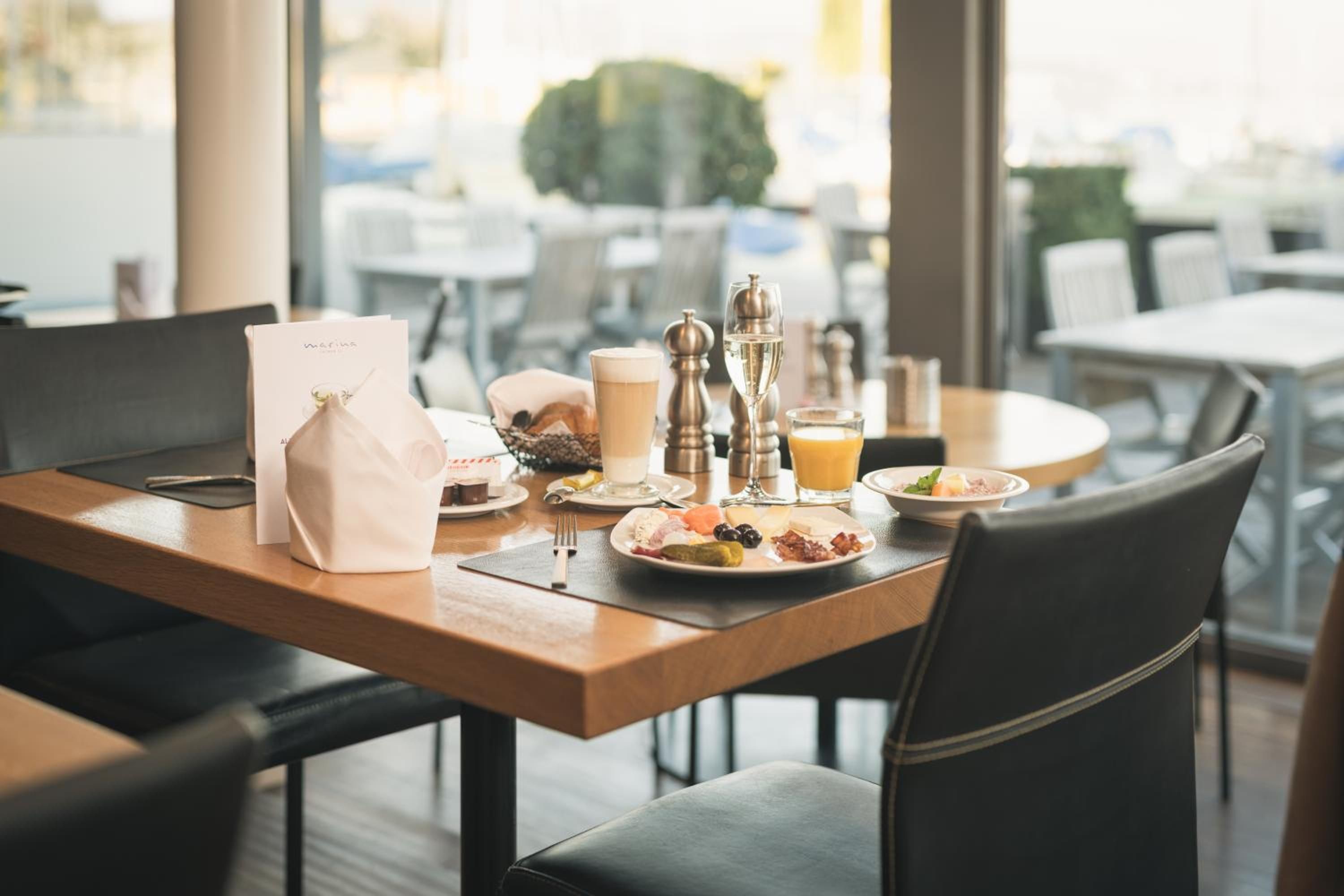 Une table de petit-déjeuner avec une table en bois, un menu, un sac, une assiette de nourriture, un verre de jus d’orange, ainsi que des salières et des poivrières.