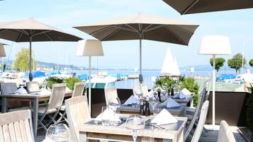 An outdoor dining area with tables, chairs, and umbrellas overlooking a marina with boats.