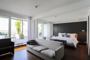 A modern hotel room with a large bed, a sofa, and a balcony with a view.