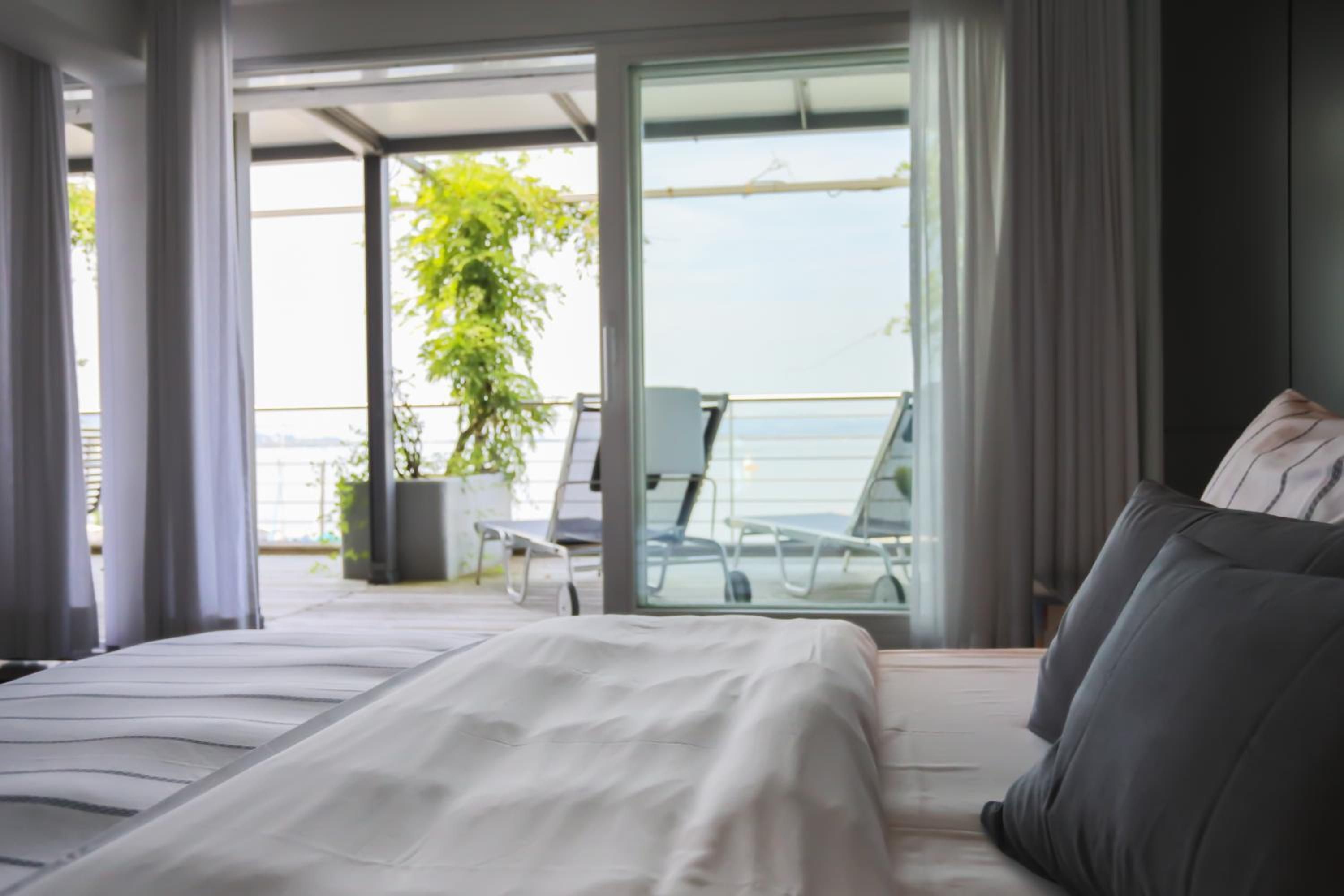 Un dormitorio moderno con una cama grande, un balcón con vistas al mar y una planta en maceta.