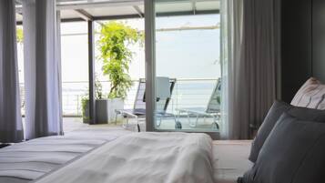 Un dormitorio moderno con una cama grande, un balcón con vistas al mar y una planta en maceta.