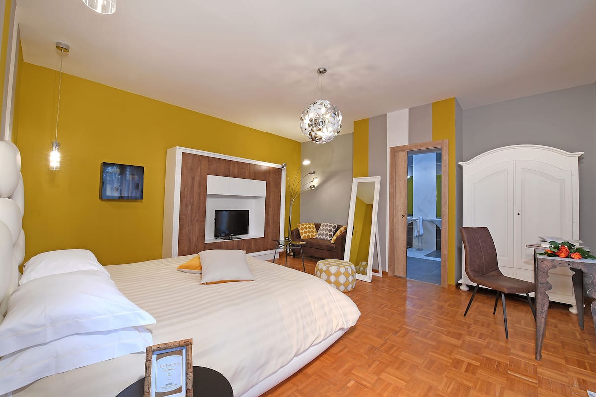 A hotel room with a bed, a TV, a sofa, a chair, and a table.