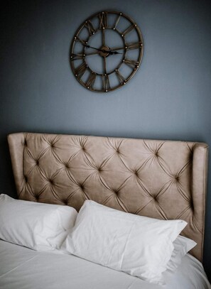Una cama con cabecera capitonada y un reloj de pared redondo.