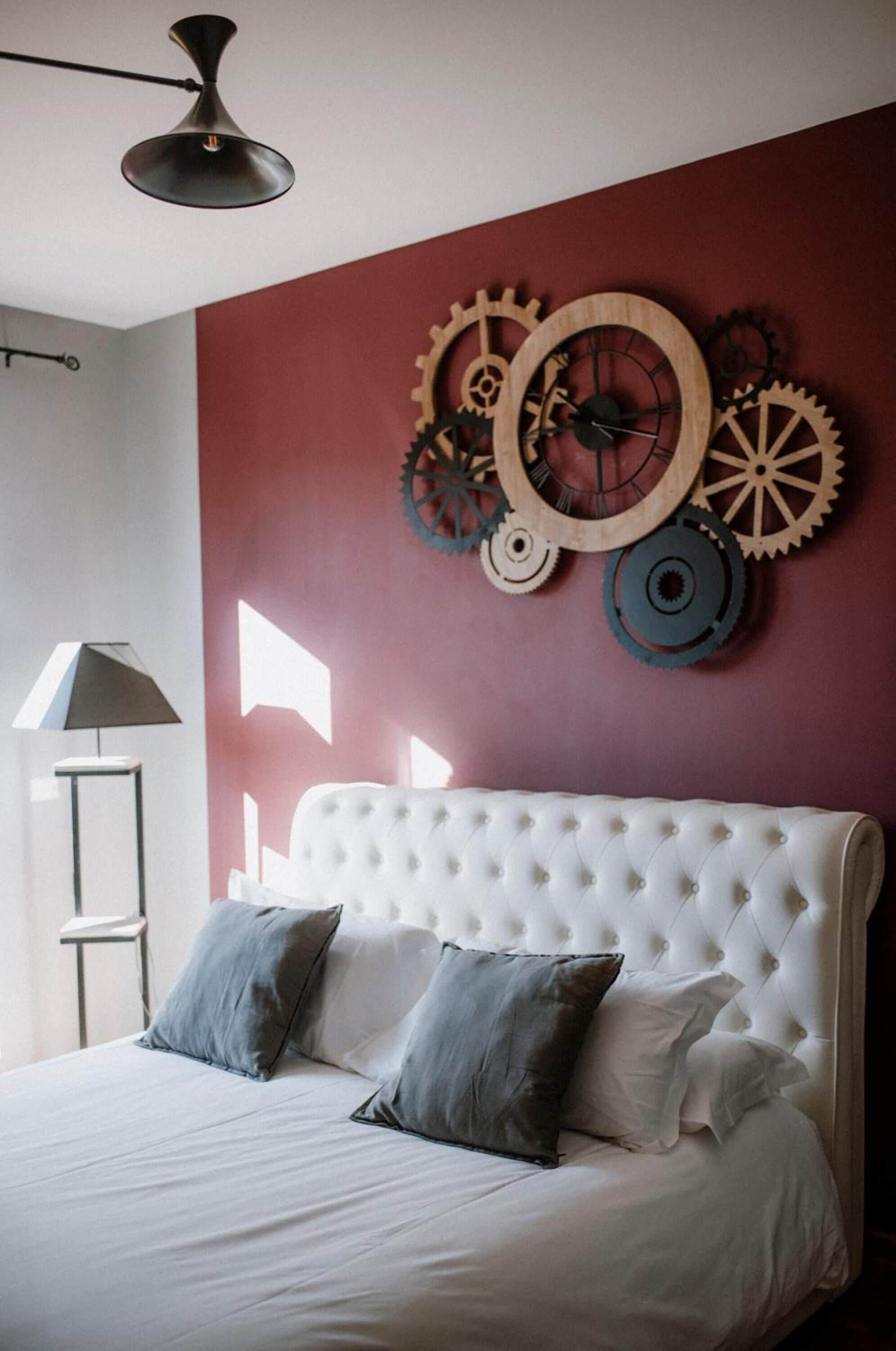 A bedroom with a white tufted headboard, two grey pillows, and a wall-mounted gear decoration.