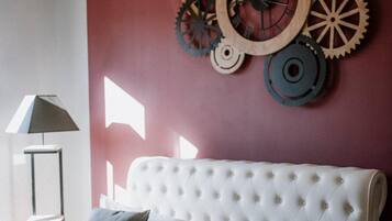 A bedroom with a white tufted headboard, two grey pillows, and a wall-mounted gear decoration.
