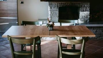 A dining area with a wooden table and chairs, a stone fireplace, and a hanging light fixture.