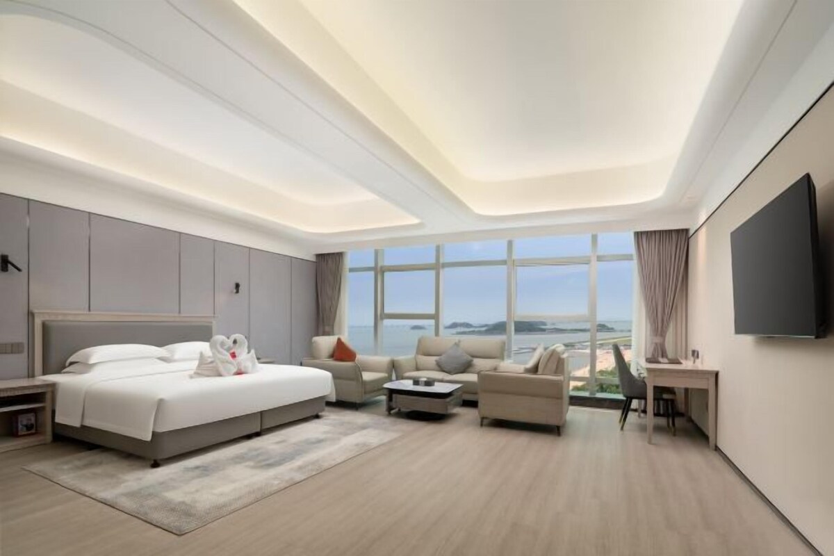 A modern hotel room with a large bed, two sofas, a desk, and a TV.