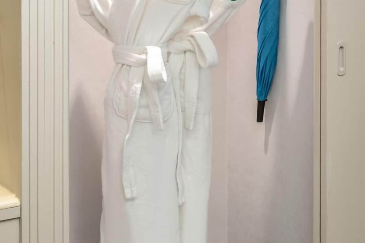 A white bathrobe hanging on a door with a blue umbrella beside it.