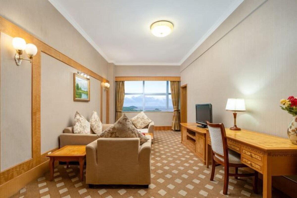 Ein Hotelzimmer mit Sofa, Schreibtisch, Fernseher und einem Fenster mit Blick.