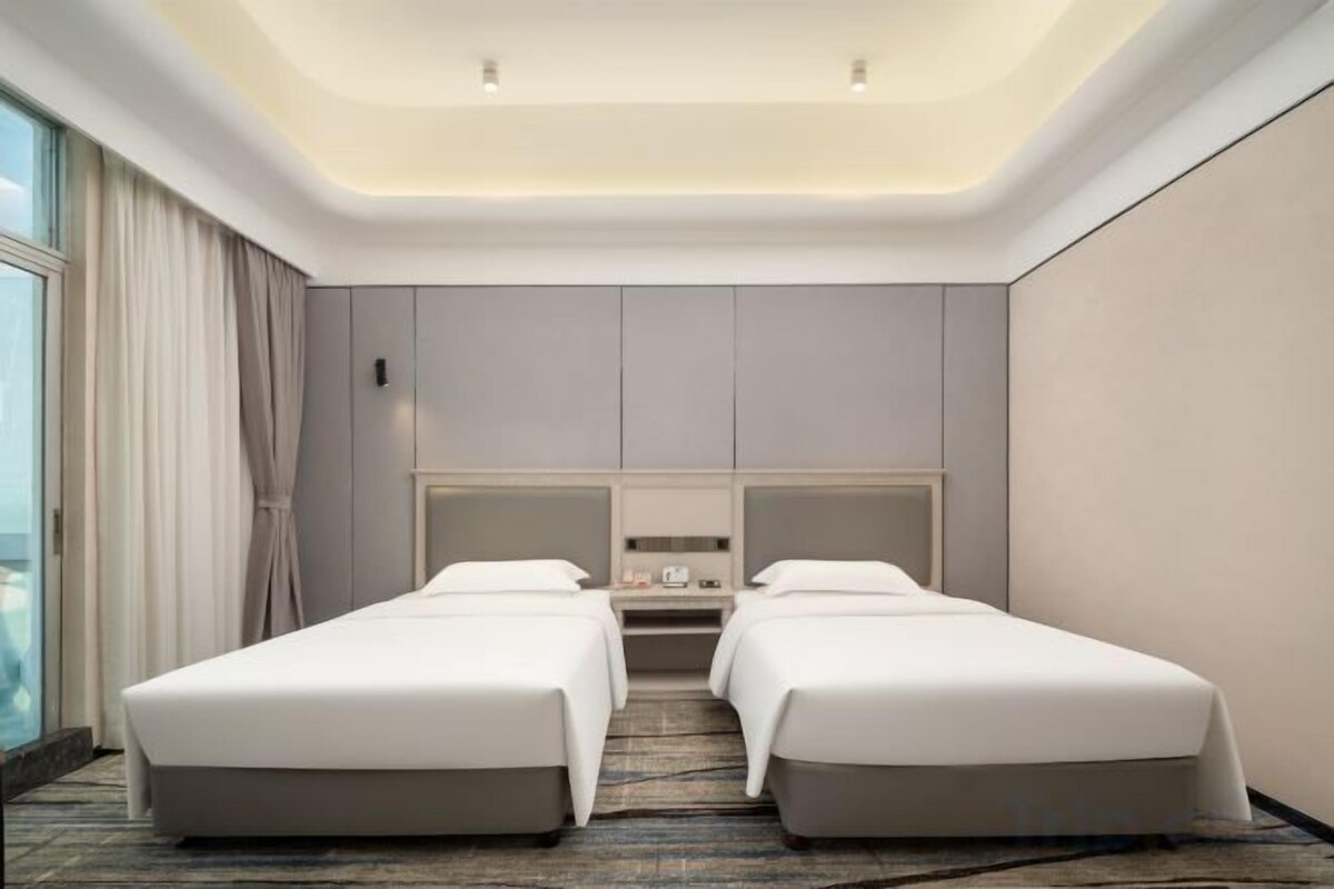 Una habitació d'hotel amb dos llits, una finestra gran i un disseny modern al sostre.