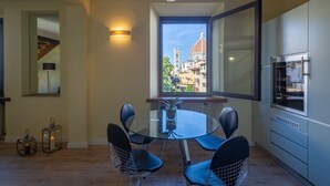 Un coin repas avec une table ronde en verre, des chaises noires, une vue sur un dôme et des bâtiments, et une cuisine moderne équipée d’un réfrigérateur.