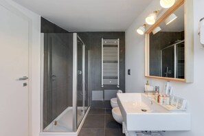 A modern bathroom with a glass shower enclosure, a white sink with toiletries, and a large mirror.