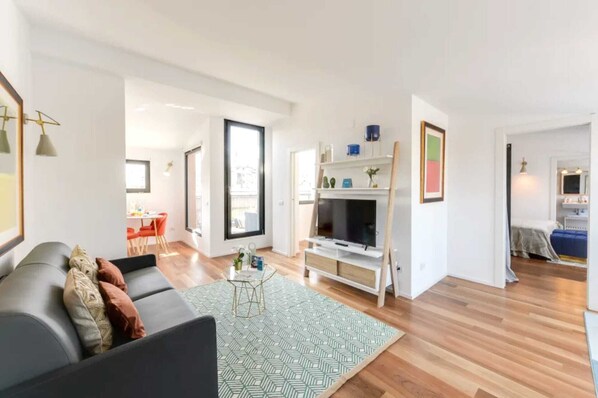 A modern living room with a sofa, TV stand, and a dining area with chairs.