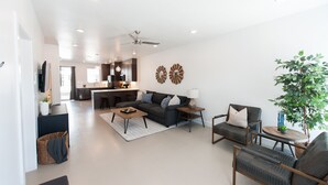 A modern living room with a sofa, coffee table, and chairs, a kitchen in the background, and a ceiling fan. - New poolside Luxury townhouse in The Lofts (St. George)