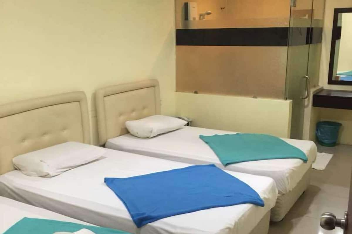 A hotel room with two beds, a glass shower enclosure, and a visible air conditioning unit.