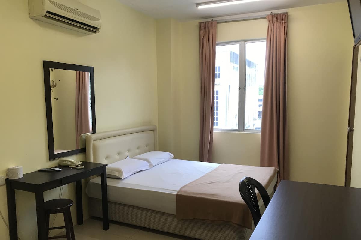 A hotel room with a bed, a desk, a chair, a mirror, and a window with curtains.