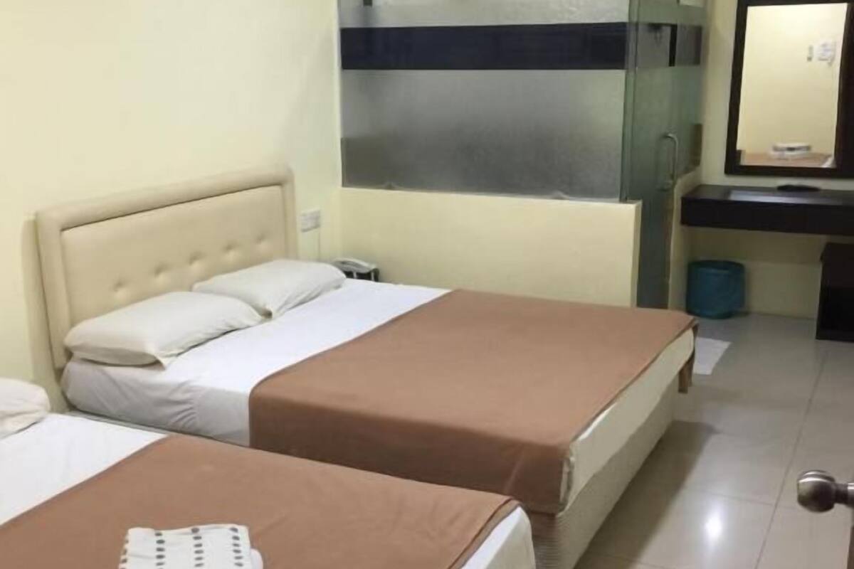 A hotel room with two beds, a bathroom with a mirror, and an air conditioning unit on the wall.