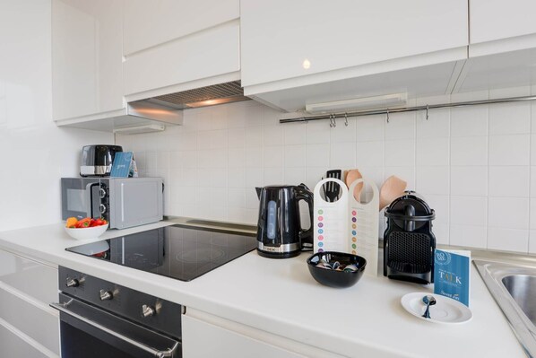 Eine moderne Küche mit weißen Schränken, einem eingebauten Ofen, einer Mikrowelle, einem Wasserkocher, einer Kaffeemaschine und einer Fruchtschale.