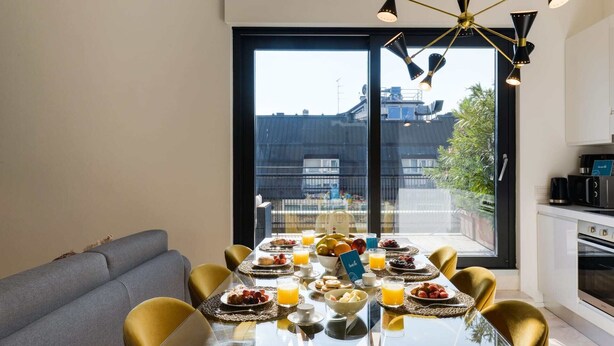 Zona pranzo moderna con tavolo in vetro, sedie gialle e un divano.
