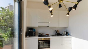 Una cucina moderna con mobili bianchi, forno a incasso, macchina del caffè e lavello. Si vedono due sedie e un tavolo da pranzo.