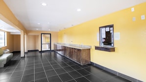A hotel lobby with a reception desk, a bench, and a door leading to another room. - Southern Comfort Hotel (Tulsa)