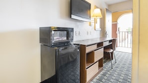 A compact kitchenette with a microwave, a small refrigerator, a wooden desk, a chair, and a TV mounted on the wall. - Southern Comfort Hotel (Tulsa)