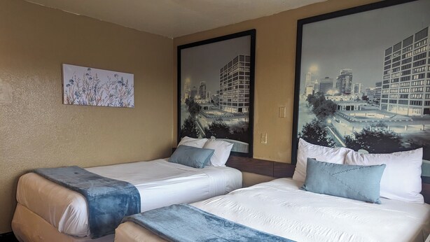 A hotel room with two beds, beige walls, and large windows with cityscape views. - Southern Comfort Hotel (Tulsa)