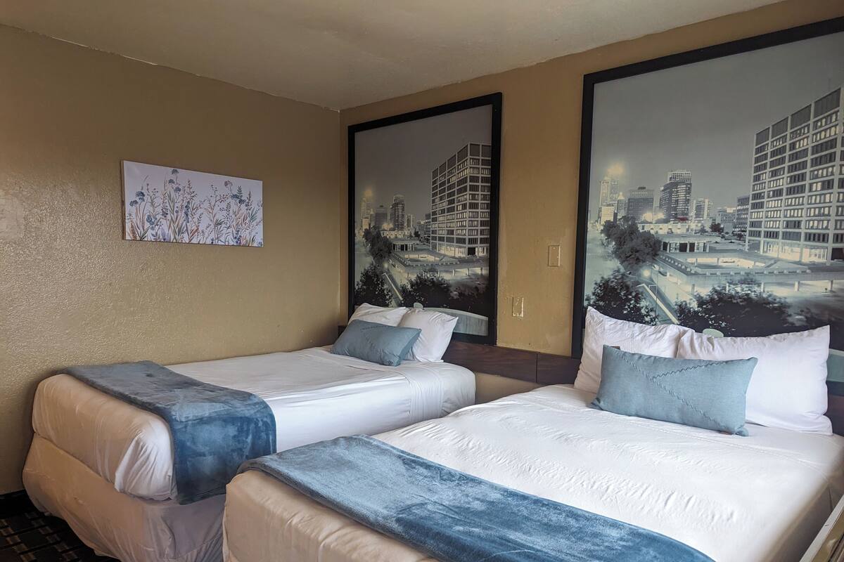 A hotel room with two beds, beige walls, and large windows with cityscape views.