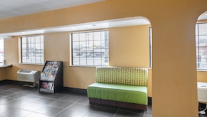A waiting area with a green sofa, a magazine rack, and large windows with a view of the street. - Southern Comfort Hotel (Tulsa)